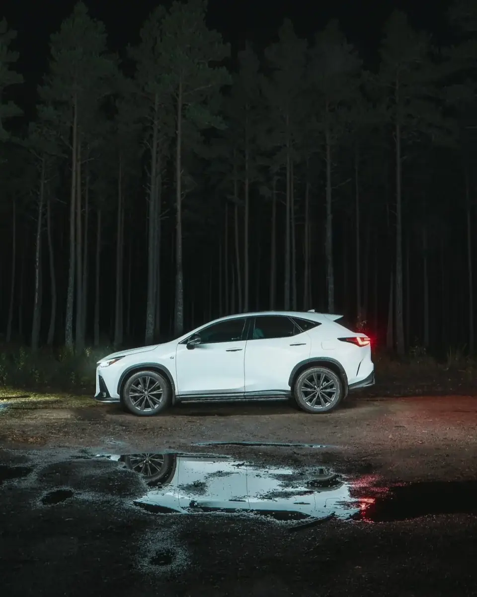White Lexus beside a forest reflected in a puddle