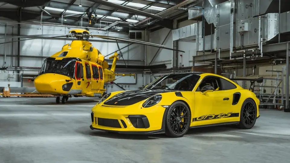 Yellow Porsche 911 GT3 RS parked in a hangar beside a yellow helicopter